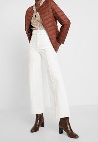 Brown puffer jacket, patterned shirt, white wide-leg pants, and glossy brown ankle boots with a block heel. Textured materials and clean lines.