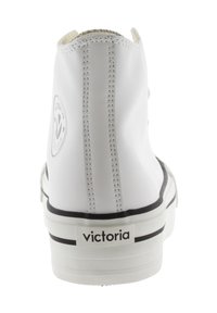 Baskets montantes blanches avec une texture lisse, rayures noires sur la semelle et un logo circulaire. Couture visible à l'arrière.