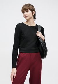 Μαύρο μακρυμάνικο τοπ με στρογγυλή λαιμόκοψη, σε συνδυασμό με μπορντό παντελόνια με μαύρα κουμπιά στο πλάι και μαύρη υφασμάτινη τσάντα.