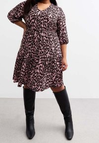 Schwarz und pinkes Tierfellmuster-Kleid mit V-Ausschnitt, Dreiviertelärmel und gestuftem Rock. Kombiniert mit kniehohen schwarzen Stiefeln.