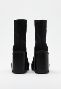 Botines negros con parte superior de tejido elástico y gruesos tacones de bloque texturizados. Los detalles de costura en la parte trasera realzan el diseño.