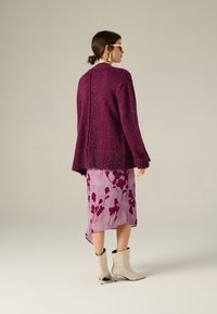 Cardigan a maglia texture viola con una cucitura sul retro, abbinato a una gonna aderente color lavanda con un motivo floreale e stivaletti crema.