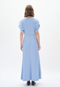 Abito lungo in tessuto azzurro chiaro con una texture liscia, dotato di maniche puff corte e vita definita, con un orlo inferiore dritto.