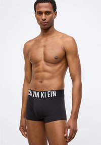 Μαύρα βαμβακερά μποξεράκια με ευρύ ελαστικό ζωνάκι που φέρει την ένδειξη "CALVIN KLEIN" σε λευκά γράμματα. Κλασικός σχεδιασμός, στενή εφαρμογή, ελάχιστοι λεπτοί σχεδιασμοί.