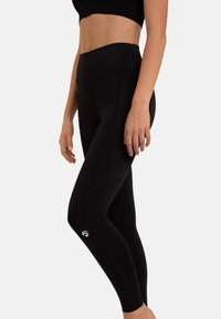Zwarte leggings met hoge tailleband, gladde textuur en logo op het onderbeen. Fitted ontwerp, geschikt voor sportkleding of casual gebruik.