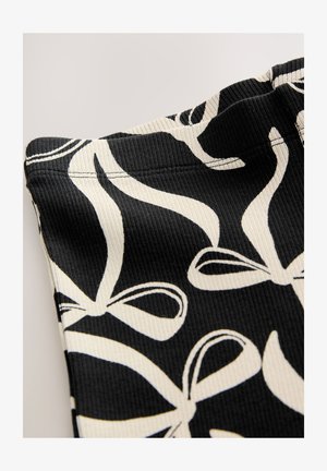 Tissu noir côtelé présentant un motif de nœuds blancs. Affiché en angle, mettant en valeur la texture et les détails de la couture.