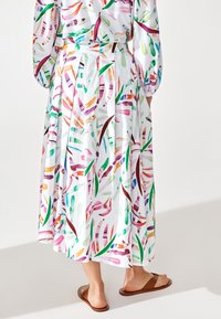 Falda maxi con un vibrante patrón de hojas multicolores sobre un fondo blanco, hecha de una tela ligera, con un diseño fluido y cintura elástica.