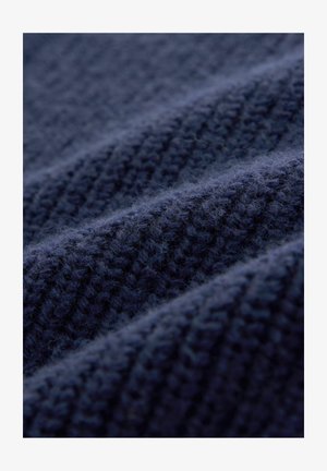 Marineblåt strikket stof med teksturerede riller, der viser en blød, fluffy overflade og et ensartet vævemønster gennem hele materialet.
