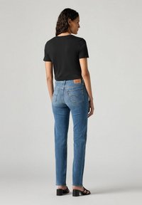 Czarny t-shirt z krótkim rękawem połączony z jasnoniebieskimi dżinsami, z klasycznym krojem i subtelnymi detalami w szyciu. Model nosi czarne sandały.