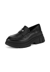 Mocasín de cuero negro con una suela gruesa, que presenta un acento metálico en forma de corazón en la parte superior y una textura suave en toda la superficie.