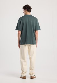 Vihreä puuvillapaita lyhyillä hihoilla, rento leikkaus ja pyöreä kaula-aukko, yhdistettynä luonnonvalkoisiin löysiin housuihin ja rentoihin lenkkareihin.