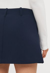 Siniharmaa skort, jossa on liehuva muotoilu, sileä pinta ja kaksi vyölenkkiä. Kangas näyttää olevan kevyt ja hengittävä.