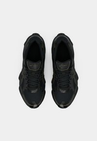 Sapatos desportivos pretos com parte superior em malha e sintético, ponta arredondada, sola texturizada e sistema de atacadores, com uma marcação discreta na lingueta.