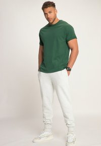 Groen T-shirt met korte mouwen, lichtgrijze sweatpants en witte sneakers. Casual pasvorm met een zachte textuur. Horloge om de pols.