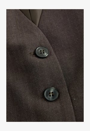 Braunstoff mit grober Textur, der zwei dunkle Knöpfe mit jeweils vier Löchern zeigt, die auf der Vorderseite einer Jacke angebracht sind.