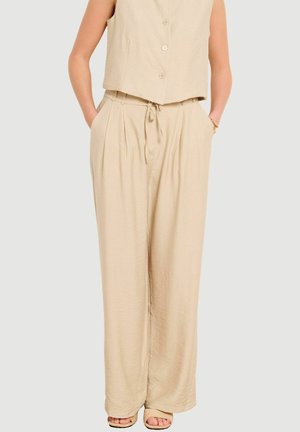 Beige wide-leg pants with a drawstring waist, side pockets, and a buttoned sleeveless top worn with open-toe sandals.