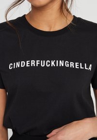 Svart bomulls t-shirt med fet vit text "CINDERFUCKINGRELLA" centrerad på bröstet. Kort ärm, rund halsringning och standard passform.