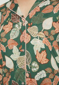 Grünes Hemd mit Knopfleiste und einem Blättermuster in Orange-, Creme- und Brauntönen. Weicher Stoff mit Kragen und leichten Paspelierungen.