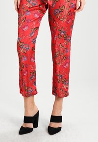 Röda blommiga byxor i slätt tyg, med uppvikt fåll och intrikata rosa och blå blommönster. Matchas med svarta klackskor med blockklack.