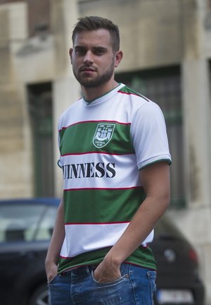 Groen en wit gestreept shirt met rode accenten, voorzien van het 'GUINNESS' logo, ronde kraag, gedragen met blauwe denim jeans.