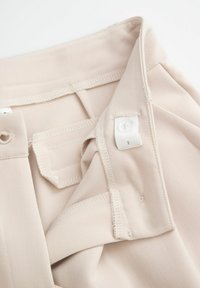 Beżowy materiałowy pasek w talii o gładkiej fakturze, z białym guzikiem i detalami w szyciu. Zawiera małą naszywkową metkę po wewnętrznej stronie.