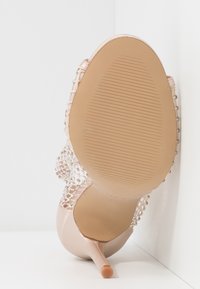 Zapato de tacón alto con parte superior de satén de color rosa claro, adornado con detalles de malla con cuentas y un delgado tacón de aguja. Suela de goma texturizada.