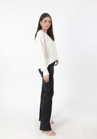 Witte oversized gebreide trui met brede mouwen, gecombineerd met strakke zwarte broeken en naaktkleurige gespjeshakken. Gladde textuur, simpel ontwerp.