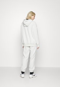 Vit fleece hoodie och matchande joggers, med avslappnad passform, ribbade ärmslut och en strukturerad yta. Bärs med sportskor.