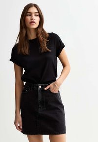 Zwart kortmouwen shirt gecombineerd met een zwarte spijkerrok. De rok heeft voorzakken en een knoopsluiting in de taille.