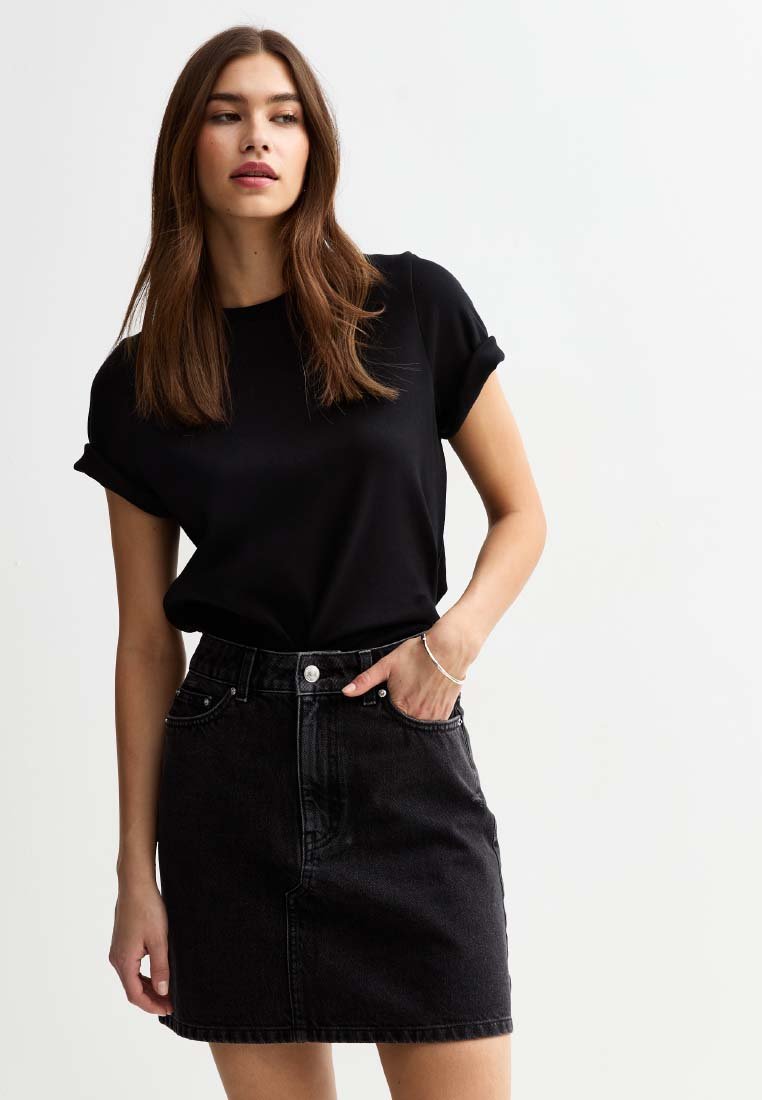 Zwart kortmouwen shirt gecombineerd met een zwarte spijkerrok. De rok heeft voorzakken en een knoopsluiting in de taille.