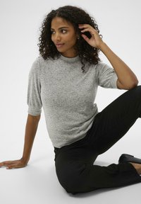 Pull en tricot gris avec un col montant, des manches courtes et une coupe décontractée. Associé à un pantalon noir. Texture lisse et design décontracté.