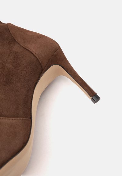 Chaussure à talon haut en daim marron avec talon stiletto fin et semelle beige sur un fond clair.
