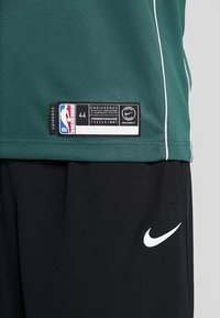 Canotta da basket in rete verde con dettagli bianchi, taglia 44, con logo NBA e etichetta Nike. Pantaloni corti neri con logo swoosh bianco di Nike.