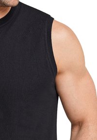 Zwarte mouwloze shirt van een gestructureerde katoenstof, met een ronde halslijn en gestikte randen, die een gespierde arm benadrukt.