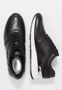 Zwarte leren sneakers met een strak ontwerp, een gestructureerd bovenwerk, een witte middenzool en metalen accenten bij de hiel en tong.