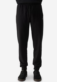 Pantalones de chándal negros hechos de una tela suave y elástica, con cintura y puños elásticos, que presentan un sutil detalle de logo en el muslo izquierdo.