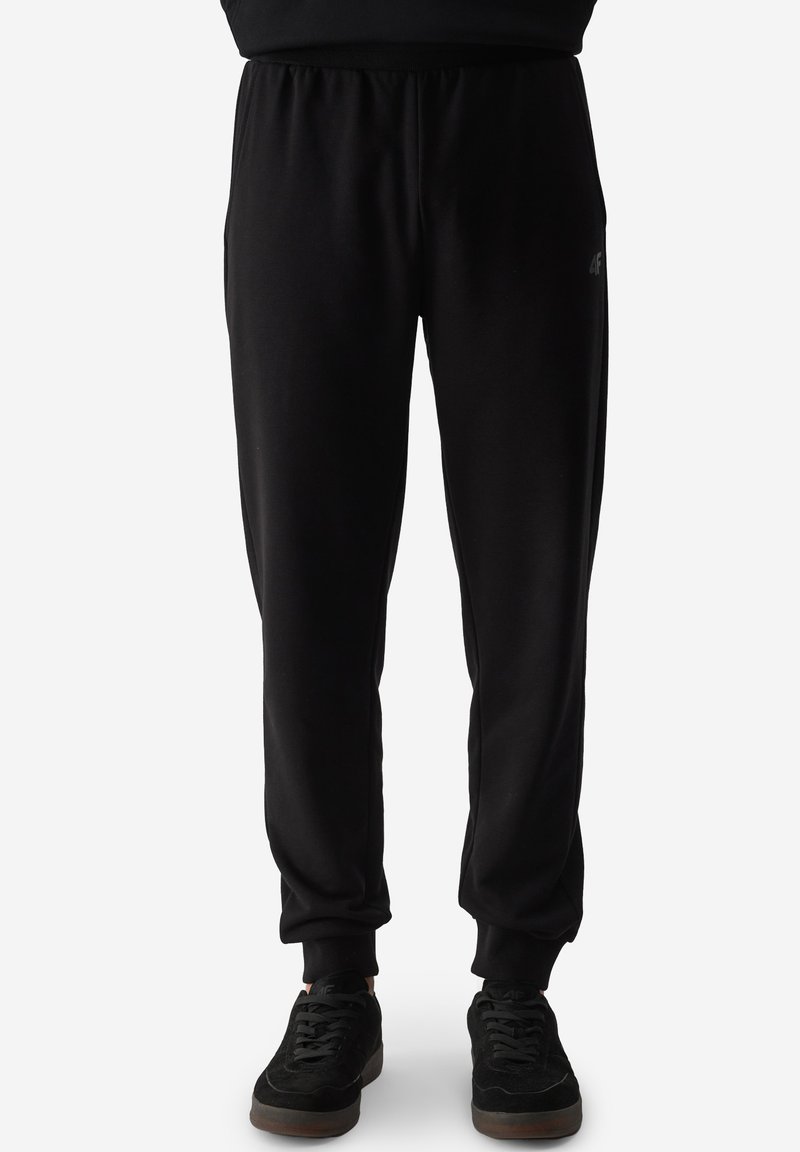 Pantalones de chándal negros hechos de una tela suave y elástica, con cintura y puños elásticos, que presentan un sutil detalle de logo en el muslo izquierdo.