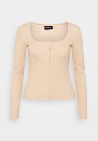 Ljust beige långärmad topp med en figurnära design. Har en fyrkantig halsringning och knäppt fram, gjord av ribbat tyg.