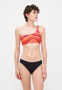 Μπικίνι τοπ ενός ώμου με πολύχρωμο σχέδιο σπείρας σε πορτοκαλί, ροζ και μοβ χρώμα, συνδυασμένο με μονόχρωμο μαύρο μπικίνι κάτω.