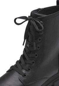 Bottines noires à lacets avec extérieur en cuir synthétique, bout rond, semelle plate et œillets en métal. Caractéristiques d'une surface texturée et de lacets en tissu.