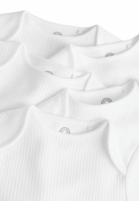 Des grenouillères blanches en coton à côtes présentent un col rond et des manches courtes, mettant en avant un design simple et minimaliste sans embellissements.