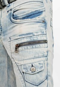 Jeans in denim azzurro chiaro caratterizzati da molteplici tasche, una tasca laterale con zip e dettagli invecchiati sul tessuto, con cuciture in contrasto.