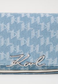 Clutch de denim azul claro con un patrón de jacquard blanco de espiga repetido y un acento plateado del logo "Karl". Cuenta con una textura elegante y suave.