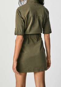 Kaki skjortklänning i mjuk bomull, med korta ärmar, en insvängd midja och en ryggsöm. Nederkanten är rak och något ovanför knäna.