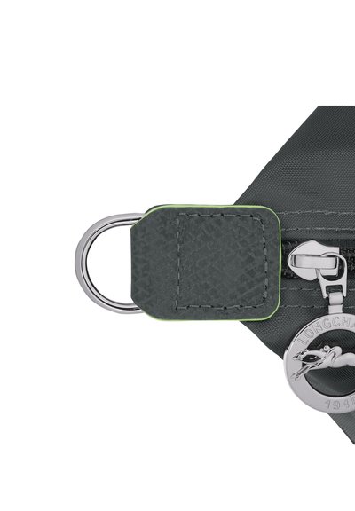 Gray fabric bag zipper with a textured black leather pull tab, green accent, and silver metal hardware including a logo charm.