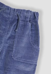 Blauwe corduroy broek met een elastische tailleband, een trekkoord en een grote zijzak aan het rechterbeen.