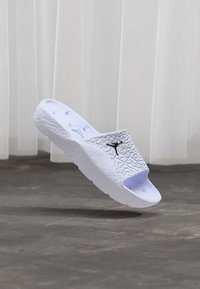 Λευκή σαγιονάρα με υφή στην επάνω πλευρά, ανοιχτή μύτη και μαύρο λογότυπο. Διαθέτει μαλακή σόλα και μινιμαλιστικό σχέδιο.