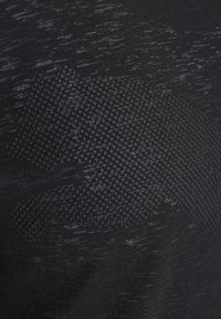 Svart atletisk tyg med ett strukturerat nätmönster i en ljusare svart nyans, med en stiliserad logotyp i ett upphöjt prickmönster.