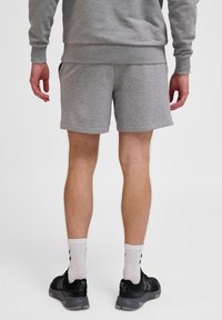Shorts gris en coton avec une taille élastique, des poches latérales et une coupe décontractée, associés à des chaussures de sport noires et des chaussettes blanches.