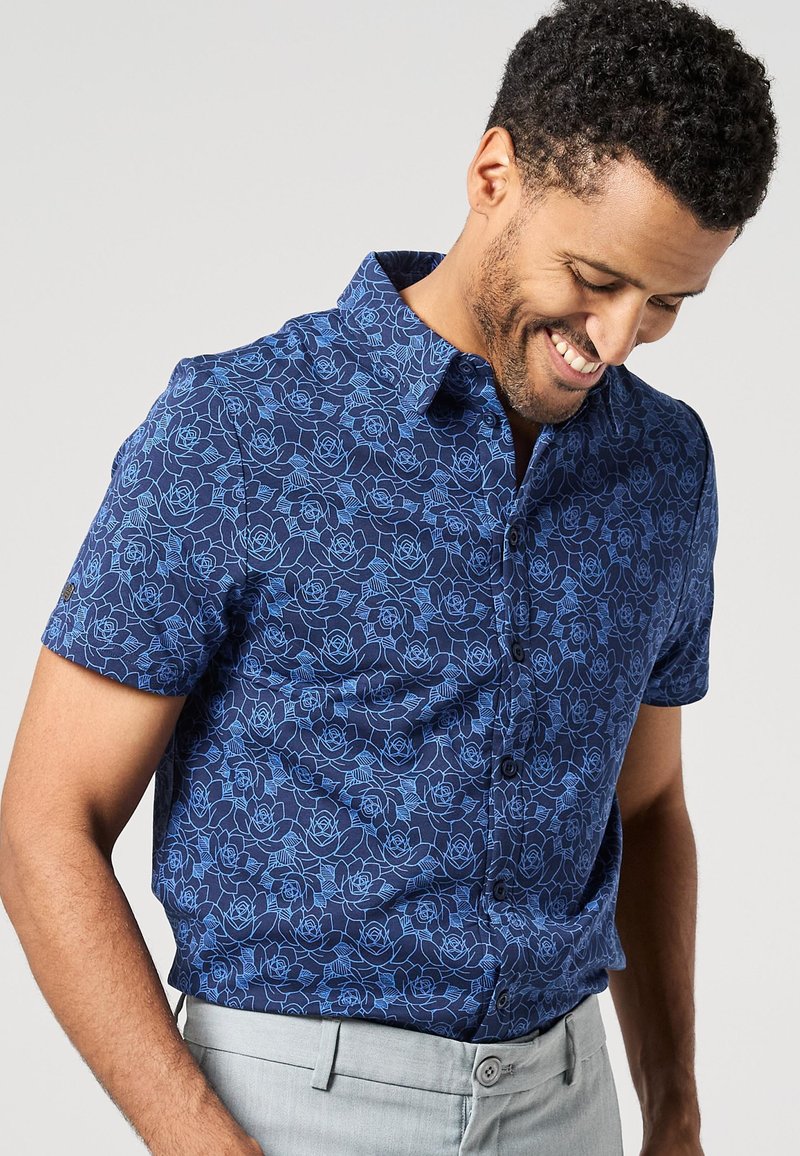 Camisa de mangas cortas en tejido azul marino con un patrón floral azul. Cuenta con cuello y cierre de botones, ofreciendo una textura suave.